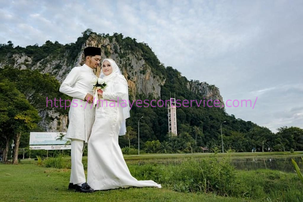Happy Malay couple in wedding attire, posing outdoors against a scenic backdrop.