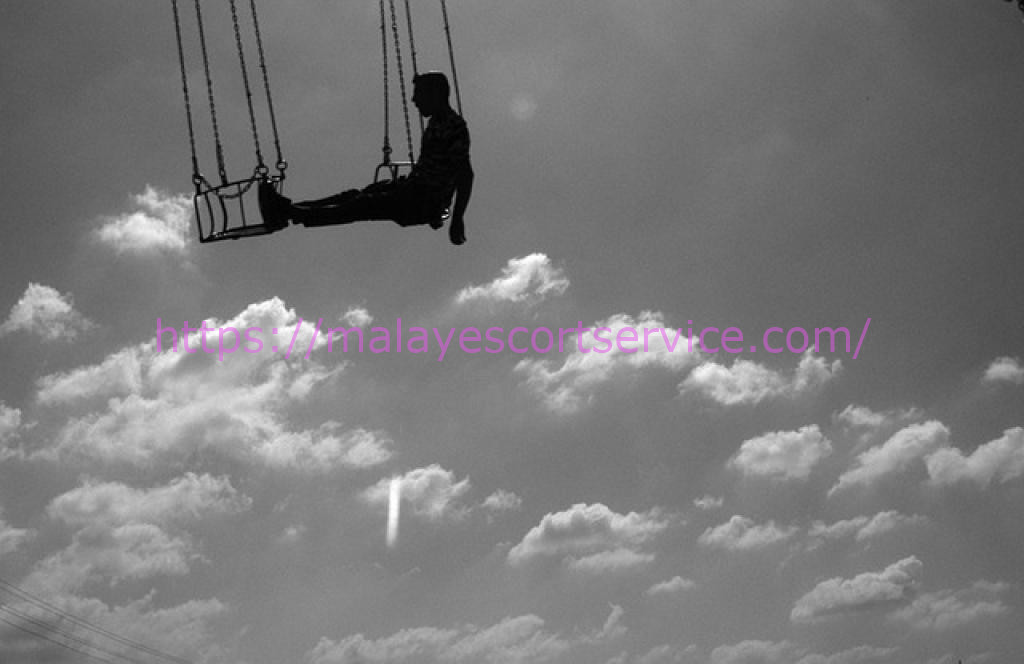 Silhouette of a person on a swing against a cloudy sky.