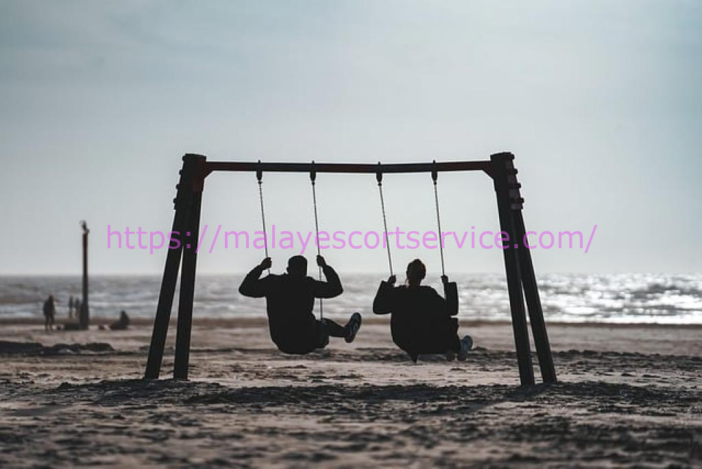 Two silhouetted figures on a swing set at the beach.