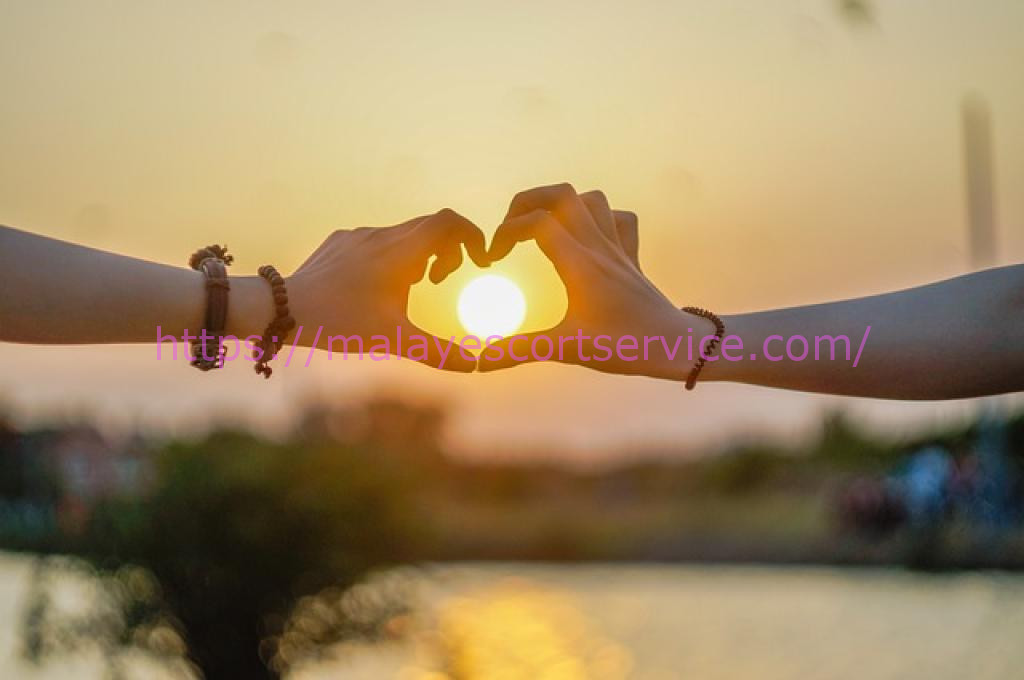 Couple forming heart shape with hands at sunset.