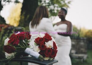 Two brides in wedding attire, bouquets of red and white roses in the foreground.