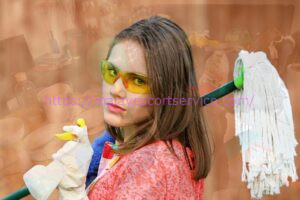 Woman cleaning with mop and spray bottle, wearing safety glasses.